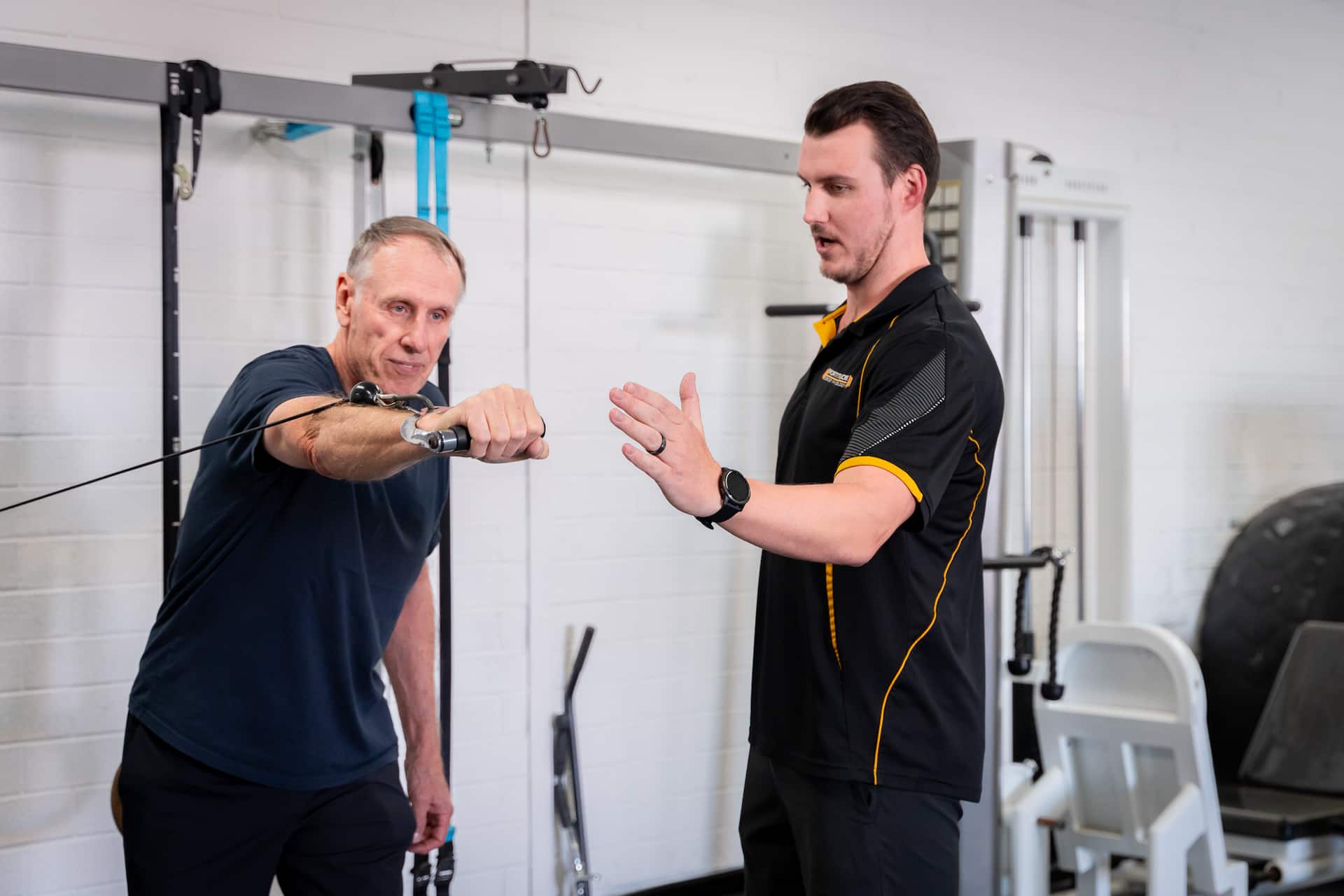 Coach helping elderly man at cable machine with post cancer exercise routine