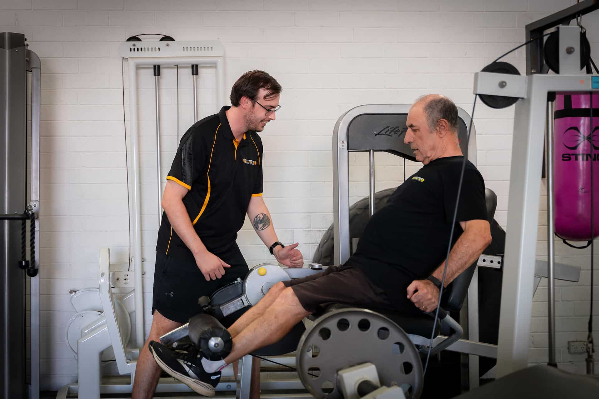 Coach helping elderly man at quad extension machine with prostate cancer exercise recommendations